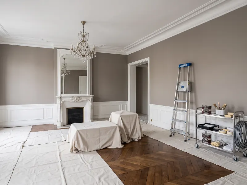 Salon aux moulures en cours de peinture, sols protégés par des bâches